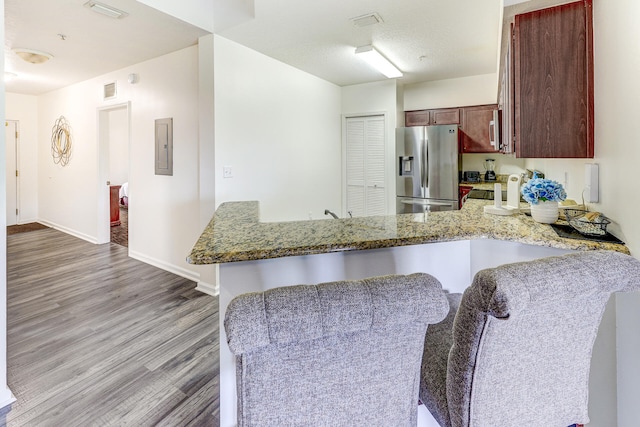 kitchen with a breakfast bar area, hardwood / wood-style floors, stainless steel fridge, light stone counters, and kitchen peninsula