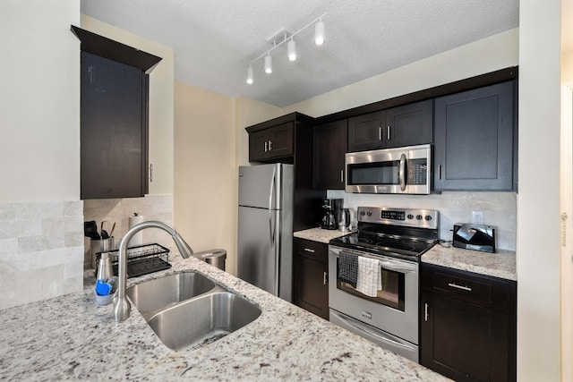 kitchen featuring track lighting, stainless steel appliances, sink, light stone countertops, and a textured ceiling