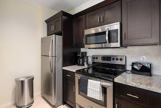 kitchen with dark brown cabinetry, light stone countertops, tasteful backsplash, and stainless steel appliances