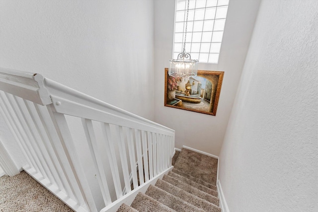 stairs with a chandelier, a textured wall, carpet flooring, and baseboards