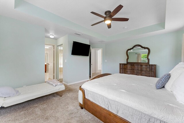 bedroom featuring ensuite bathroom, a tray ceiling, carpet, and ceiling fan