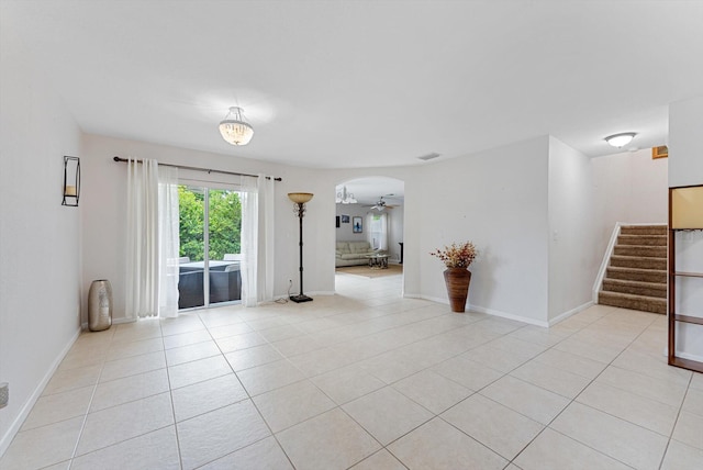 unfurnished room with arched walkways, stairway, baseboards, and light tile patterned floors