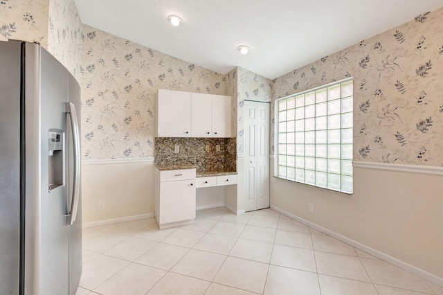 kitchen with backsplash, white cabinets, stainless steel fridge, dark stone countertops, and light tile patterned floors