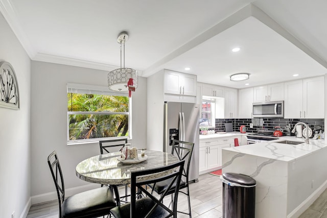 kitchen featuring appliances with stainless steel finishes, white cabinetry, a wealth of natural light, and light stone countertops