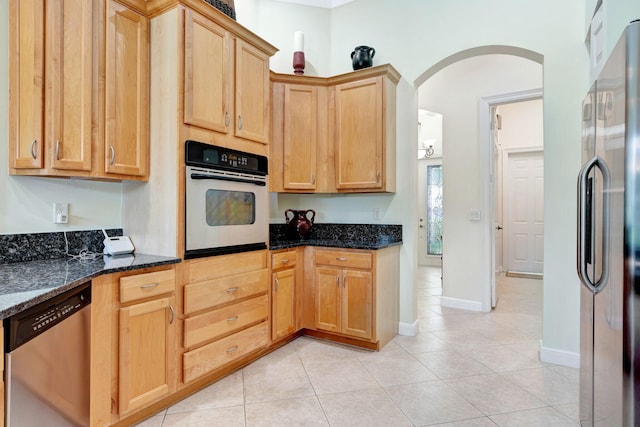 kitchen with light tile patterned floors, light brown cabinets, stainless steel appliances, and dark stone countertops