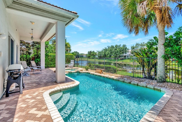 view of swimming pool with a grill, a patio area, and a water view