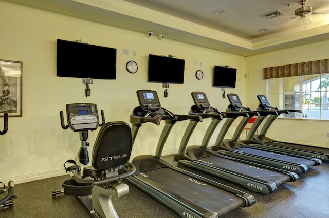 workout area with ceiling fan and a tray ceiling