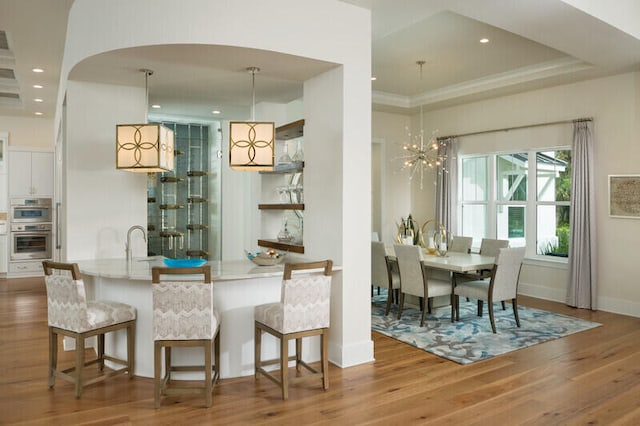 dining room featuring ornamental molding, a tray ceiling, sink, wood-type flooring, and a notable chandelier