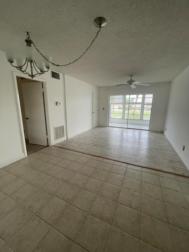 empty room featuring a textured ceiling, ceiling fan with notable chandelier, and hardwood / wood-style floors