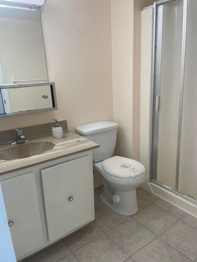 bathroom featuring tile patterned flooring, a shower with door, toilet, and vanity