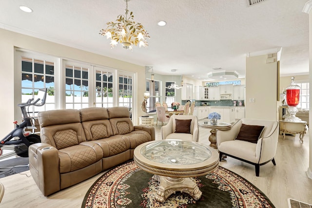 living room with plenty of natural light, ornamental molding, light hardwood / wood-style flooring, and an inviting chandelier