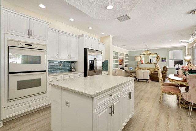 kitchen featuring stainless steel refrigerator with ice dispenser, double oven, pendant lighting, a center island, and white cabinetry