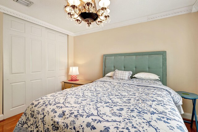 bedroom featuring a chandelier, wood-type flooring, a closet, and ornamental molding