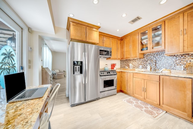 kitchen with light stone countertops, stainless steel appliances, light hardwood / wood-style floors, and sink