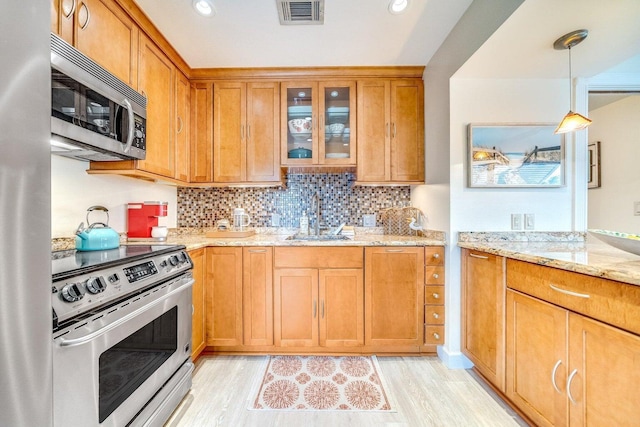 kitchen featuring sink, light stone countertops, light wood-type flooring, decorative light fixtures, and stainless steel appliances