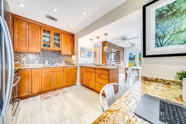 kitchen featuring decorative light fixtures, light stone counters, kitchen peninsula, and stainless steel refrigerator