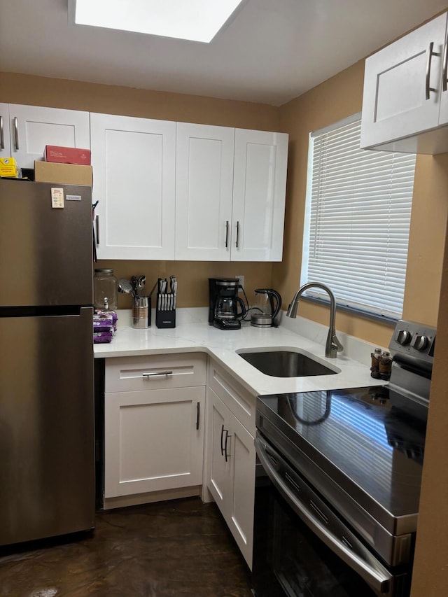 kitchen with stainless steel fridge, electric range, white cabinetry, and sink