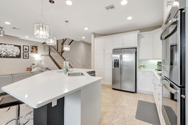 kitchen featuring sink, white cabinetry, stainless steel appliances, decorative light fixtures, and a kitchen island with sink