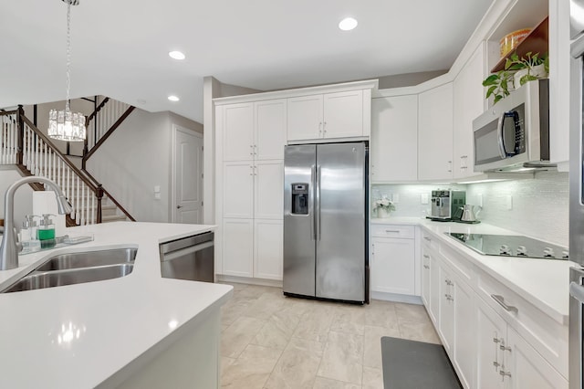 kitchen with appliances with stainless steel finishes, sink, white cabinetry, pendant lighting, and a chandelier