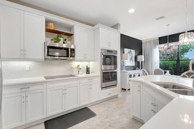 kitchen with appliances with stainless steel finishes, sink, hanging light fixtures, white cabinetry, and a notable chandelier