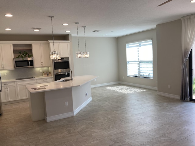 kitchen with appliances with stainless steel finishes, sink, an island with sink, white cabinetry, and decorative light fixtures