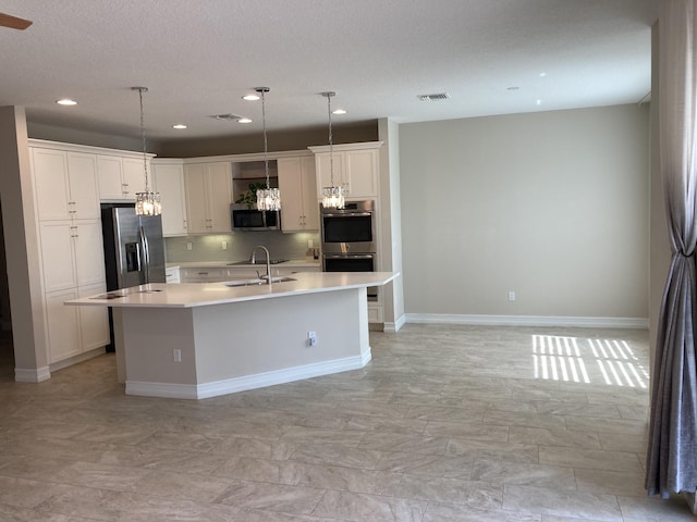 kitchen with white cabinets, stainless steel appliances, decorative light fixtures, and a kitchen island with sink