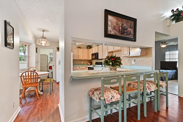 kitchen featuring decorative backsplash, electric range, a textured ceiling, pendant lighting, and a breakfast bar