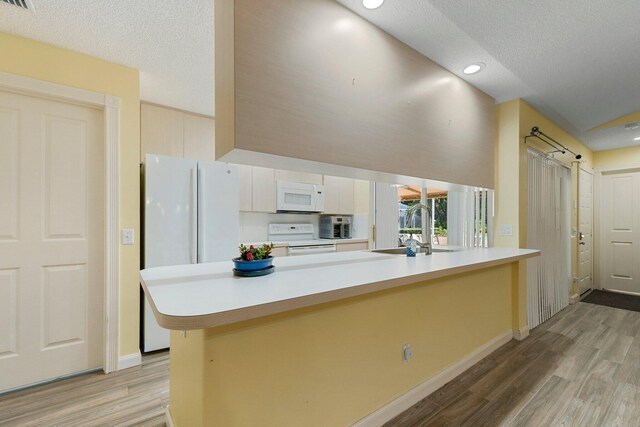 kitchen with a textured ceiling, kitchen peninsula, white appliances, and sink