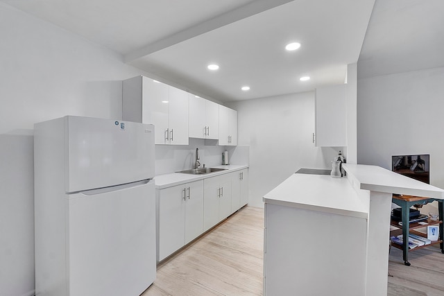 kitchen featuring white cabinetry, white refrigerator, sink, light hardwood / wood-style flooring, and kitchen peninsula