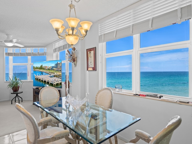 dining room with plenty of natural light, a water view, a textured ceiling, and a chandelier