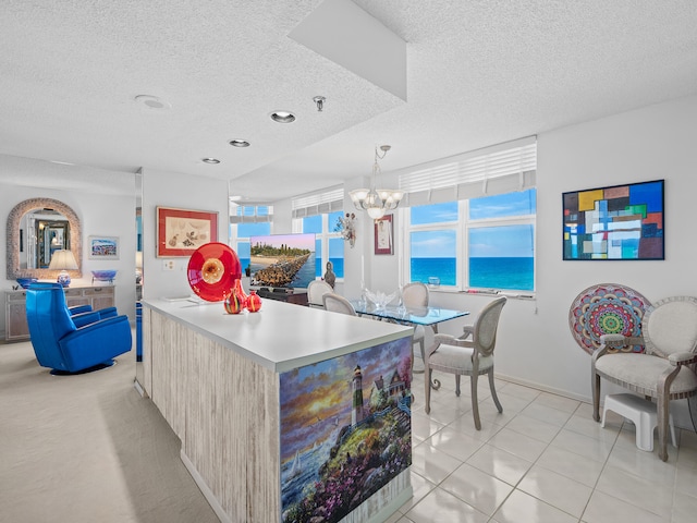 kitchen featuring light tile patterned flooring, a chandelier, a water view, pendant lighting, and a textured ceiling