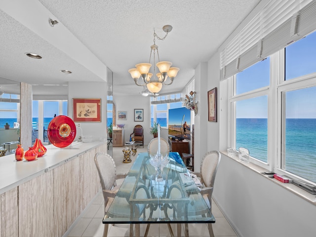 dining area featuring a water view, a textured ceiling, light tile patterned floors, and a chandelier