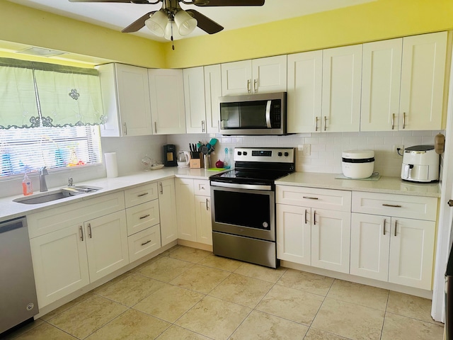 kitchen featuring appliances with stainless steel finishes, tasteful backsplash, white cabinets, sink, and ceiling fan