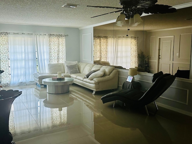 living room with ceiling fan, tile patterned floors, ornamental molding, and a textured ceiling