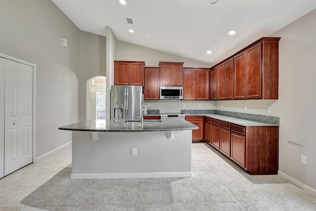 kitchen with dark stone counters, sink, appliances with stainless steel finishes, light tile patterned floors, and a kitchen island with sink