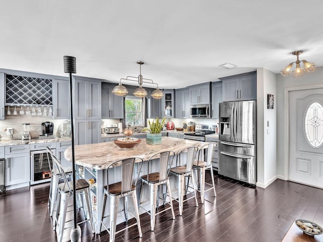 kitchen featuring stainless steel appliances, wine cooler, light stone counters, pendant lighting, and a kitchen island