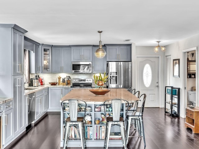 kitchen with decorative backsplash, appliances with stainless steel finishes, light stone counters, decorative light fixtures, and a kitchen island