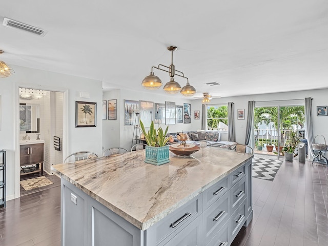 kitchen with a kitchen island, light stone countertops, hanging light fixtures, and a wealth of natural light