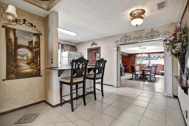 kitchen featuring a kitchen bar, stainless steel fridge, decorative light fixtures, a textured ceiling, and a chandelier