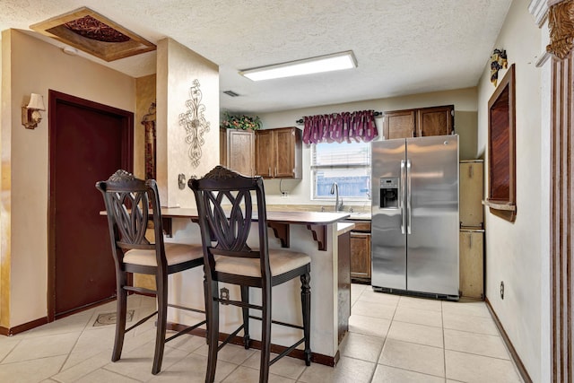 kitchen featuring kitchen peninsula, stainless steel refrigerator with ice dispenser, a textured ceiling, light tile patterned floors, and a kitchen breakfast bar