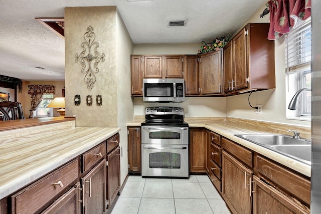 kitchen featuring appliances with stainless steel finishes, a textured ceiling, light tile patterned floors, and sink