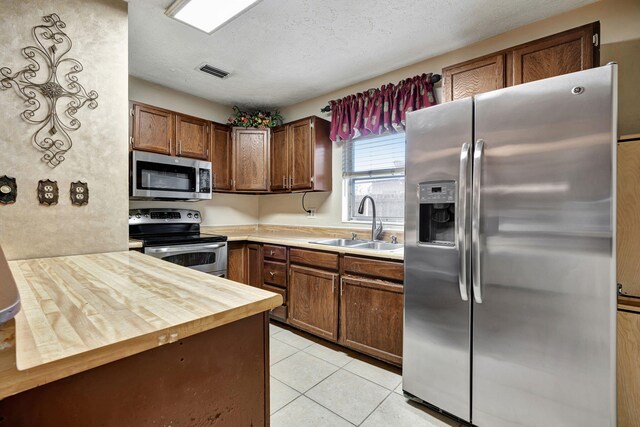 kitchen featuring light tile patterned floors, a textured ceiling, wood counters, appliances with stainless steel finishes, and sink