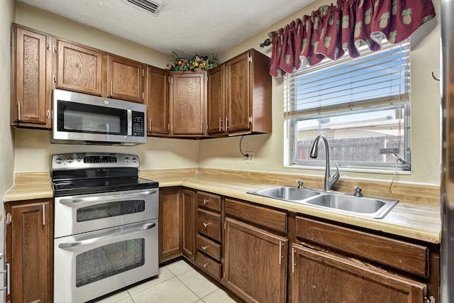 kitchen featuring light tile patterned floors, stainless steel appliances, sink, and a textured ceiling