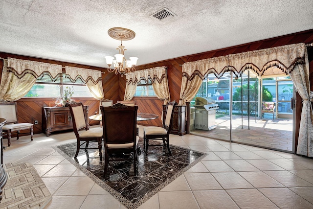 tiled dining room featuring an inviting chandelier, a textured ceiling, and wooden walls