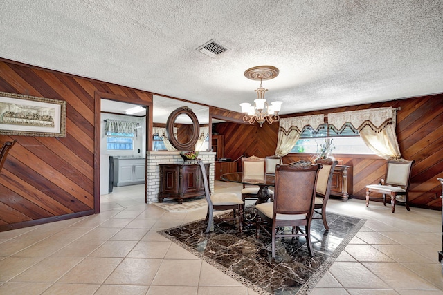 dining room with wood walls, a textured ceiling, a chandelier, and light tile patterned floors