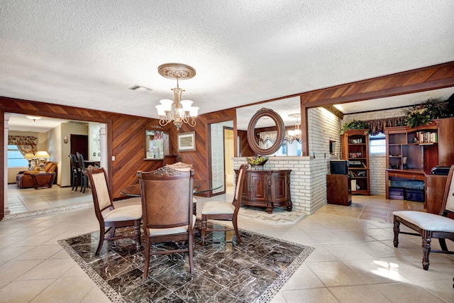 dining room featuring a healthy amount of sunlight, a textured ceiling, a chandelier, and wood walls