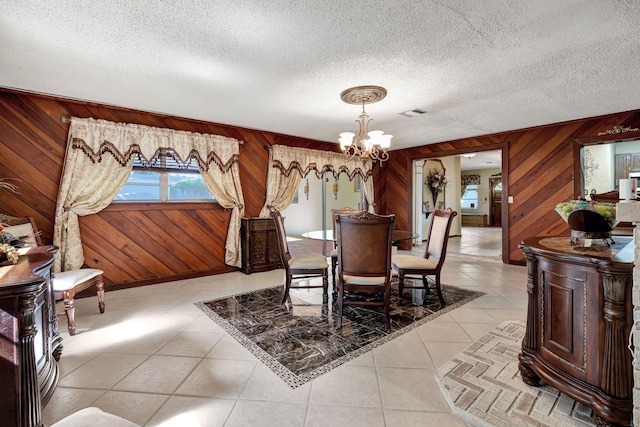 tiled dining room with wood walls, a textured ceiling, and a chandelier