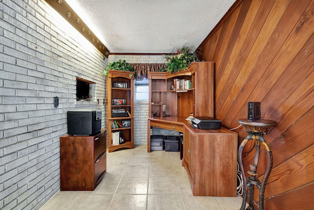 tiled office space with brick wall, wooden walls, built in desk, and a textured ceiling