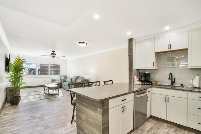 kitchen with sink, stainless steel dishwasher, dark stone counters, light hardwood / wood-style floors, and a kitchen bar