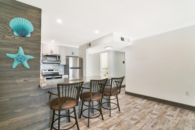 kitchen featuring white cabinetry, a kitchen breakfast bar, light hardwood / wood-style flooring, kitchen peninsula, and appliances with stainless steel finishes